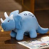 Blue plush triceratops toy with white horns and a smiling face, sitting on a table next to a newspaper.