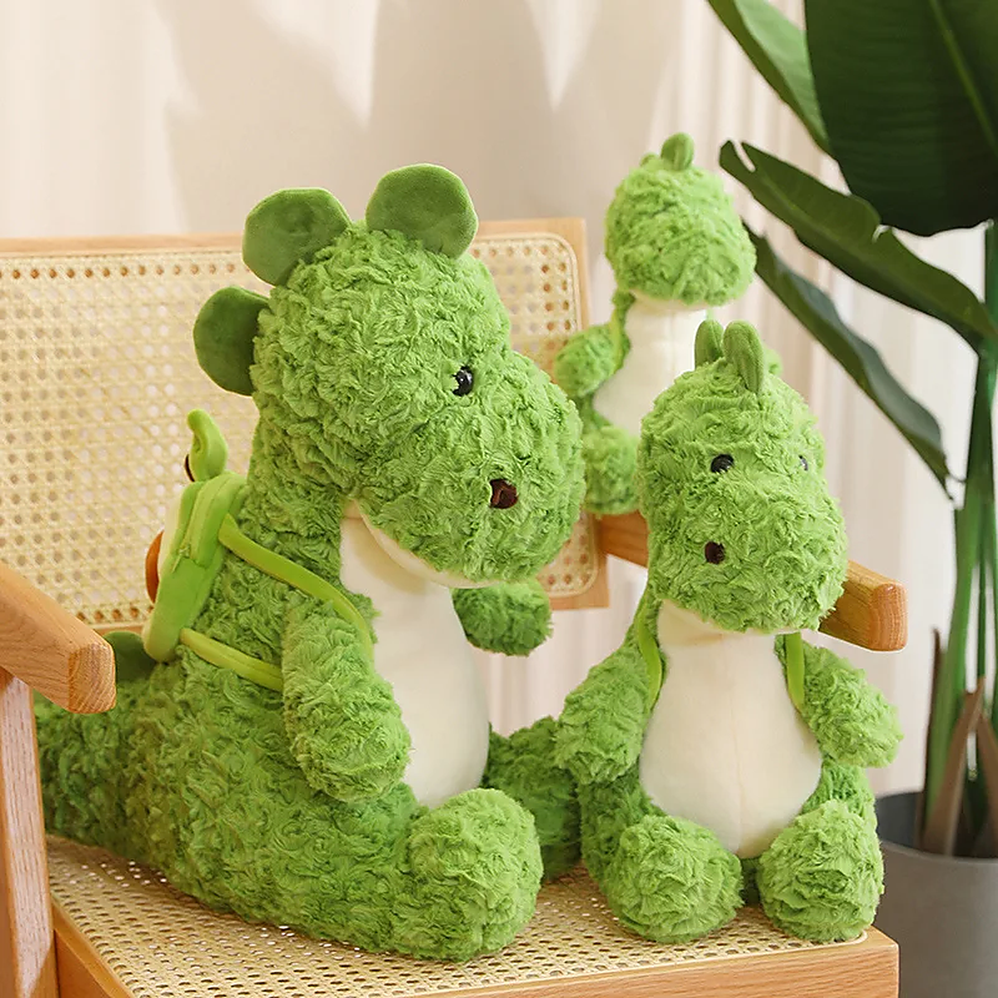Green dinosaur plush toys with textured fur, sitting on a chair, with one wearing a small avocado backpack.