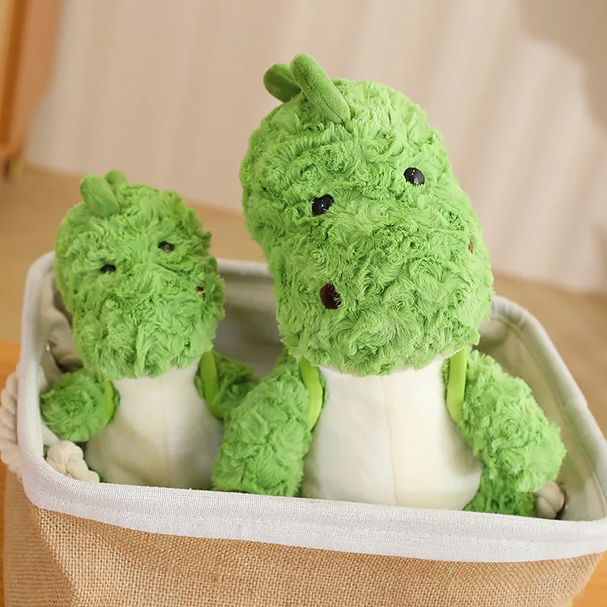 Two green dinosaur plush toys sitting together in a fabric storage basket.