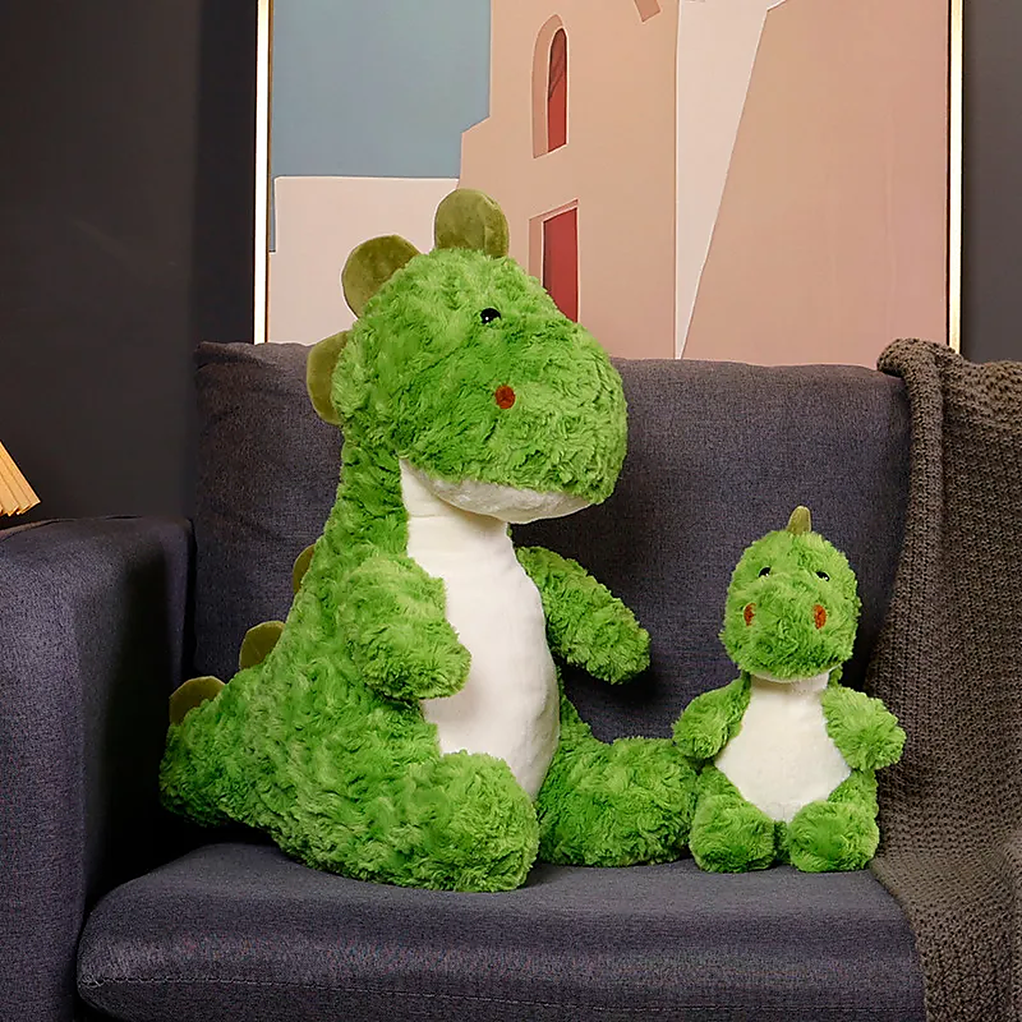 Green dinosaur plush toys, one large and one small, sitting on a dark sofa with a cozy blanket.