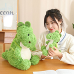 A person holds a small green dinosaur plushie while sitting next to a larger one on a table.