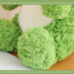 Close-up of a cute green dinosaur plush toy with soft, fluffy texture and round feet, resting on a wooden surface.