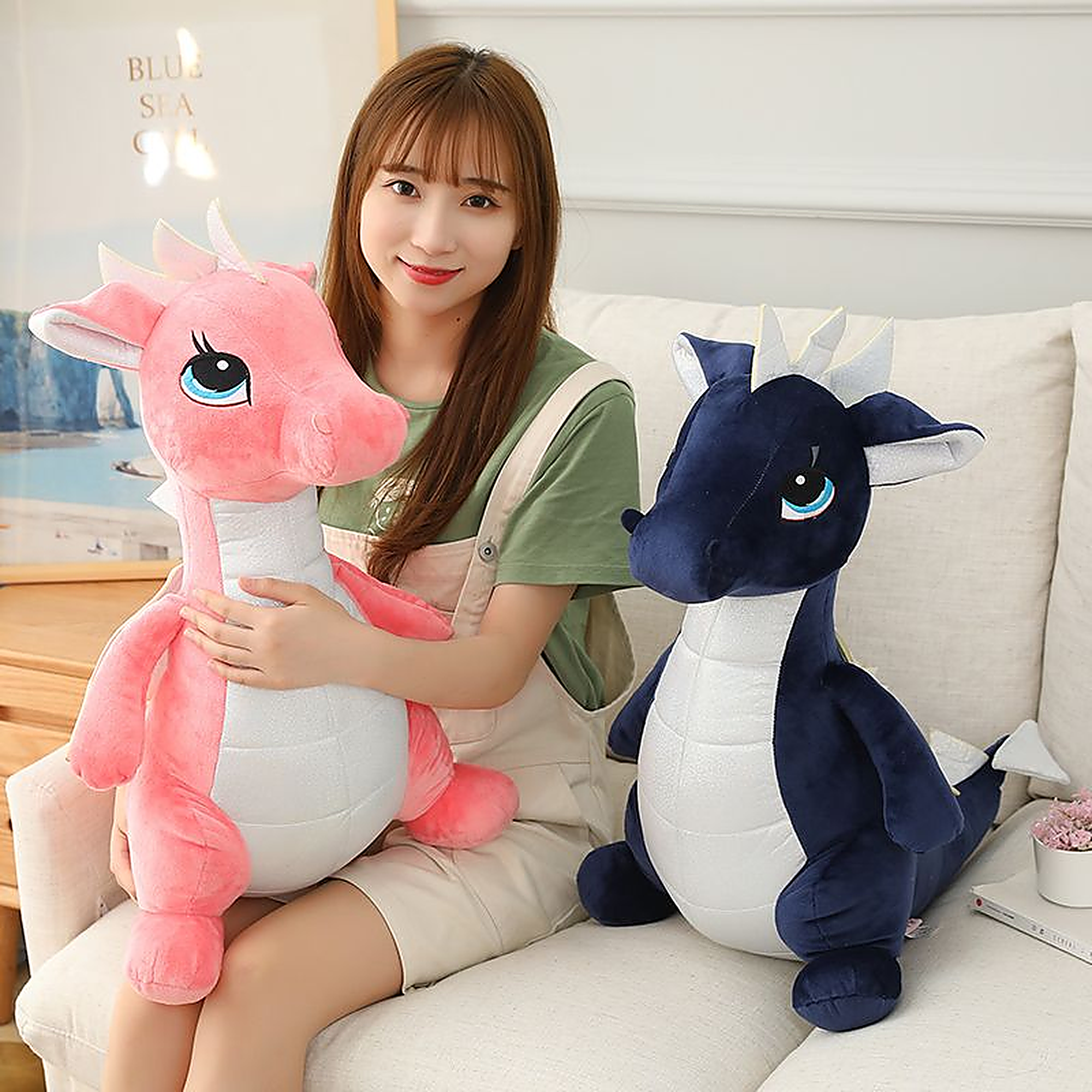 A person sits on a couch holding a pink dinosaur plush toy, with a blue dinosaur plush toy beside them.