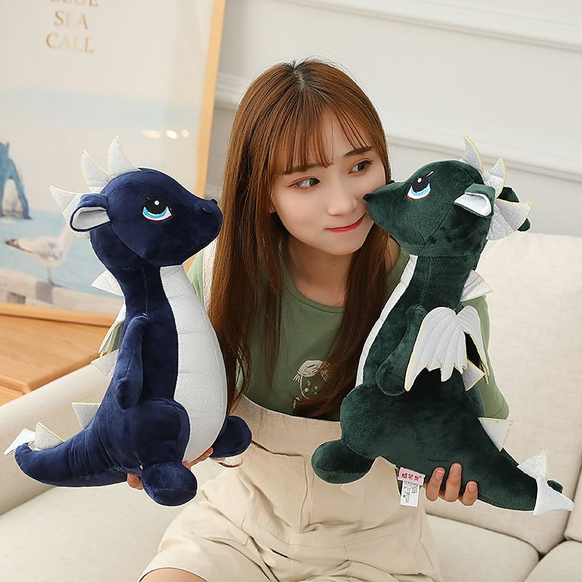 A person holds two plush dinosaur toys, one blue and one green, while sitting on a couch.