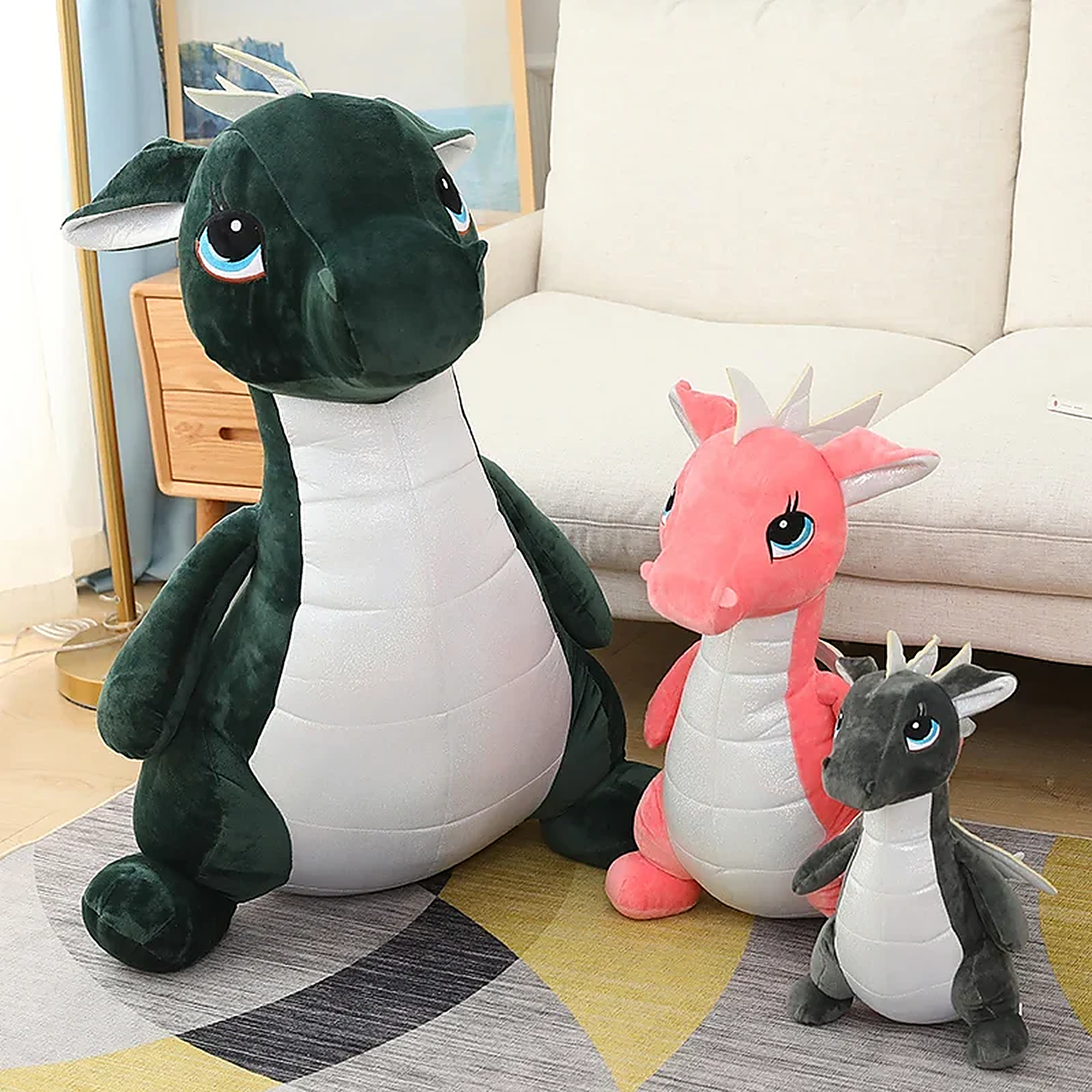 Three plush dinosaur toys in various sizes: a large green one, a medium pink one, and a small gray one, all with cute feature