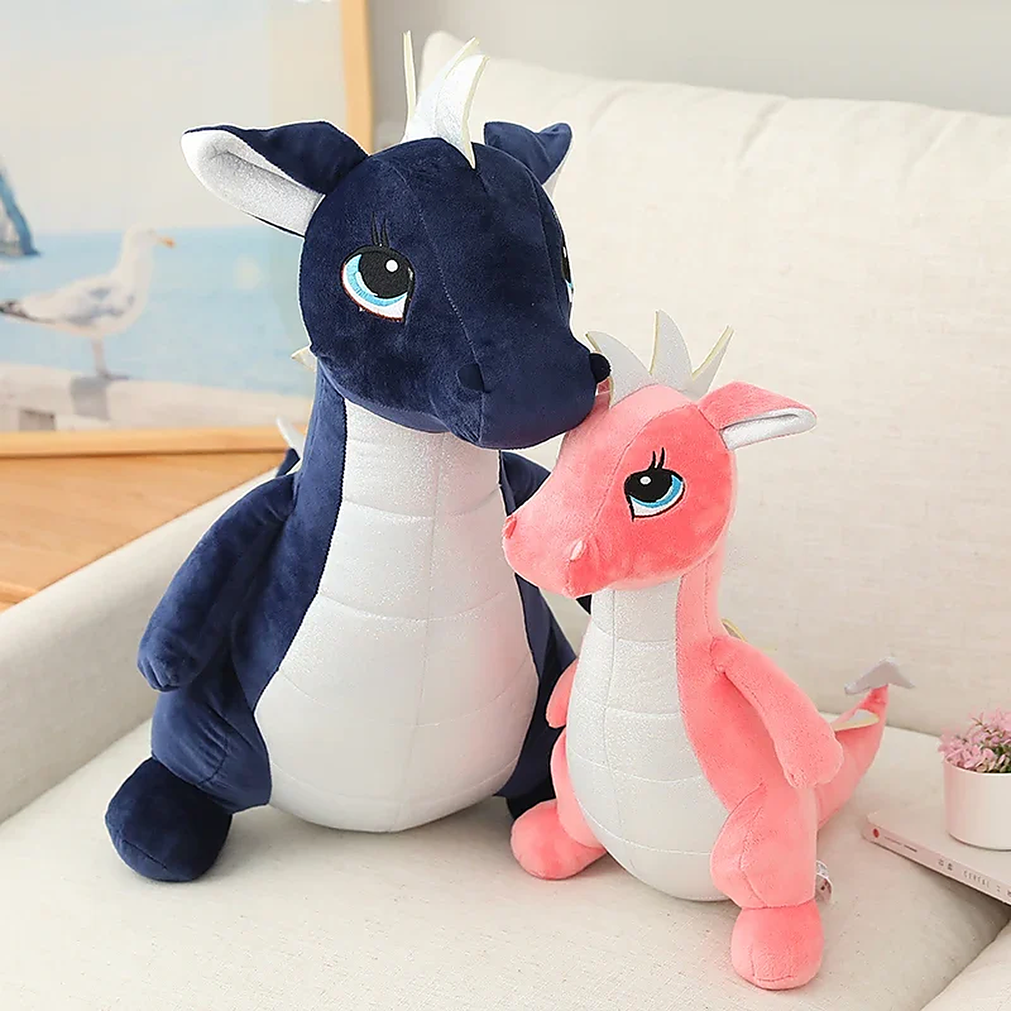 Two plush dinosaur toys, one navy blue and one pink, sitting together on a couch.