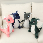 Four plush dinosaur toys in pink, blue, gray, and green, sitting on a light-colored couch.