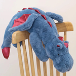 Blue plush dragon toy with red wings and accents resting on a wooden chair.