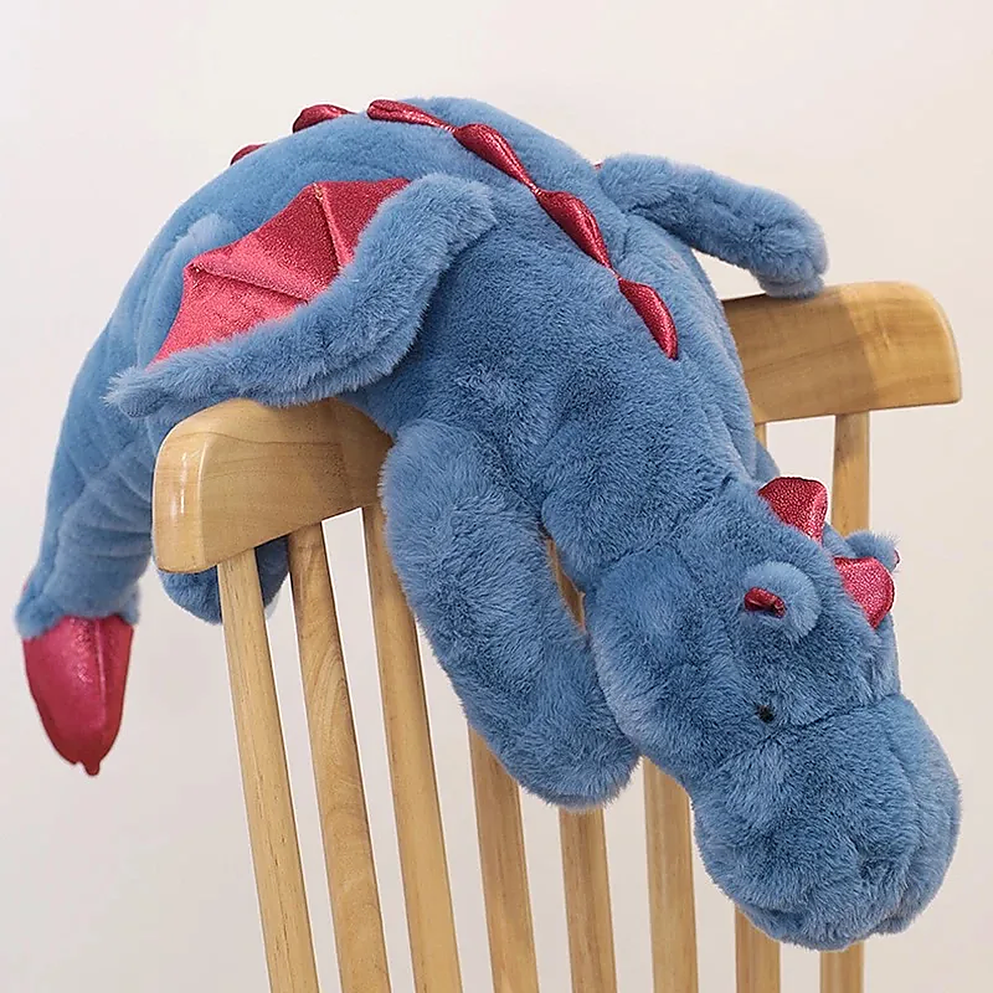 Blue plush dragon toy with red wings and accents resting on a wooden chair.