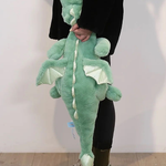 A person holds a green dragon plush toy with wings, standing against a light background.