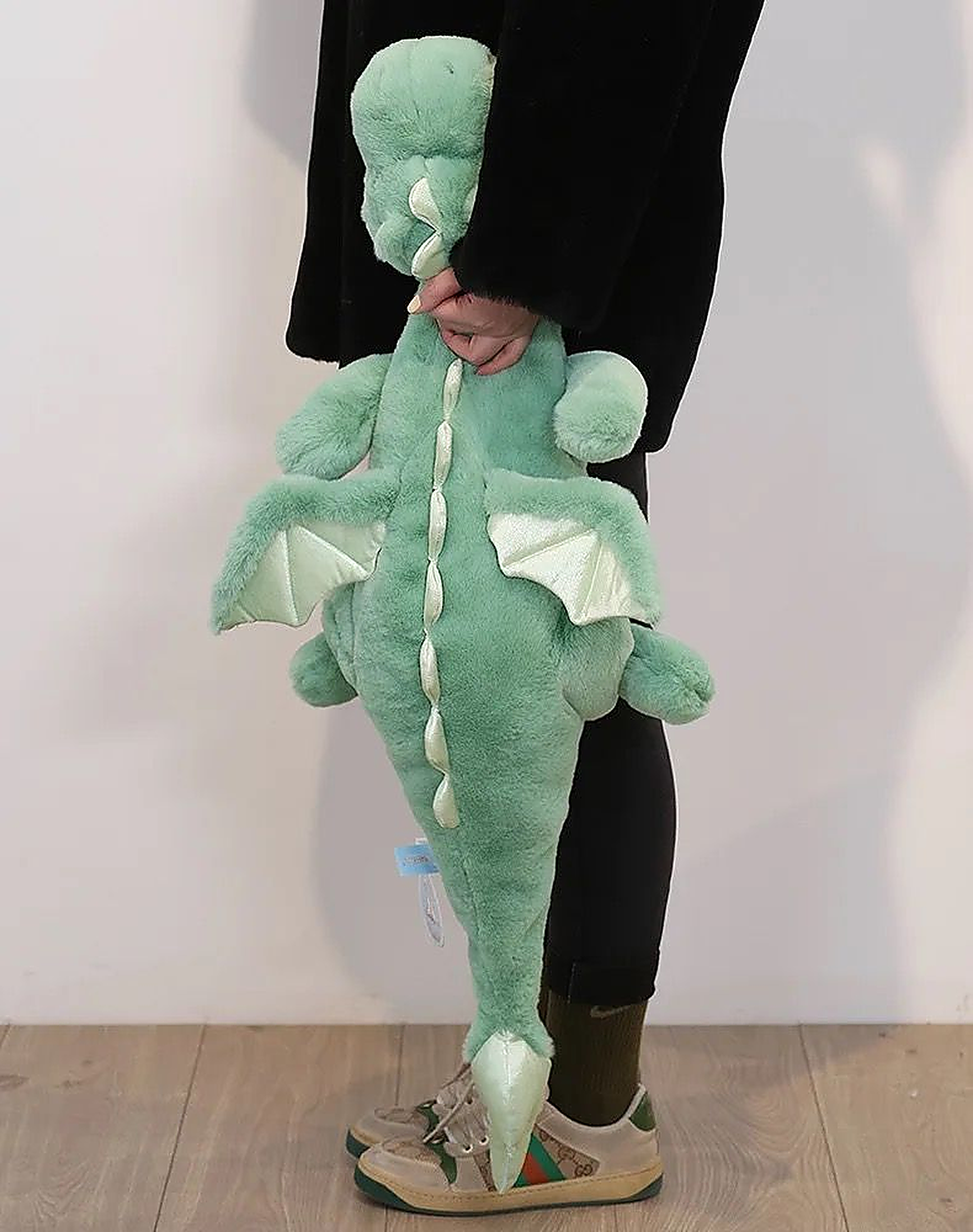 A person holds a green dragon plush toy with wings, standing against a light background.