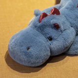 Blue dragon plush toy with red accents, featuring a round head and soft body, resting on a brown surface.