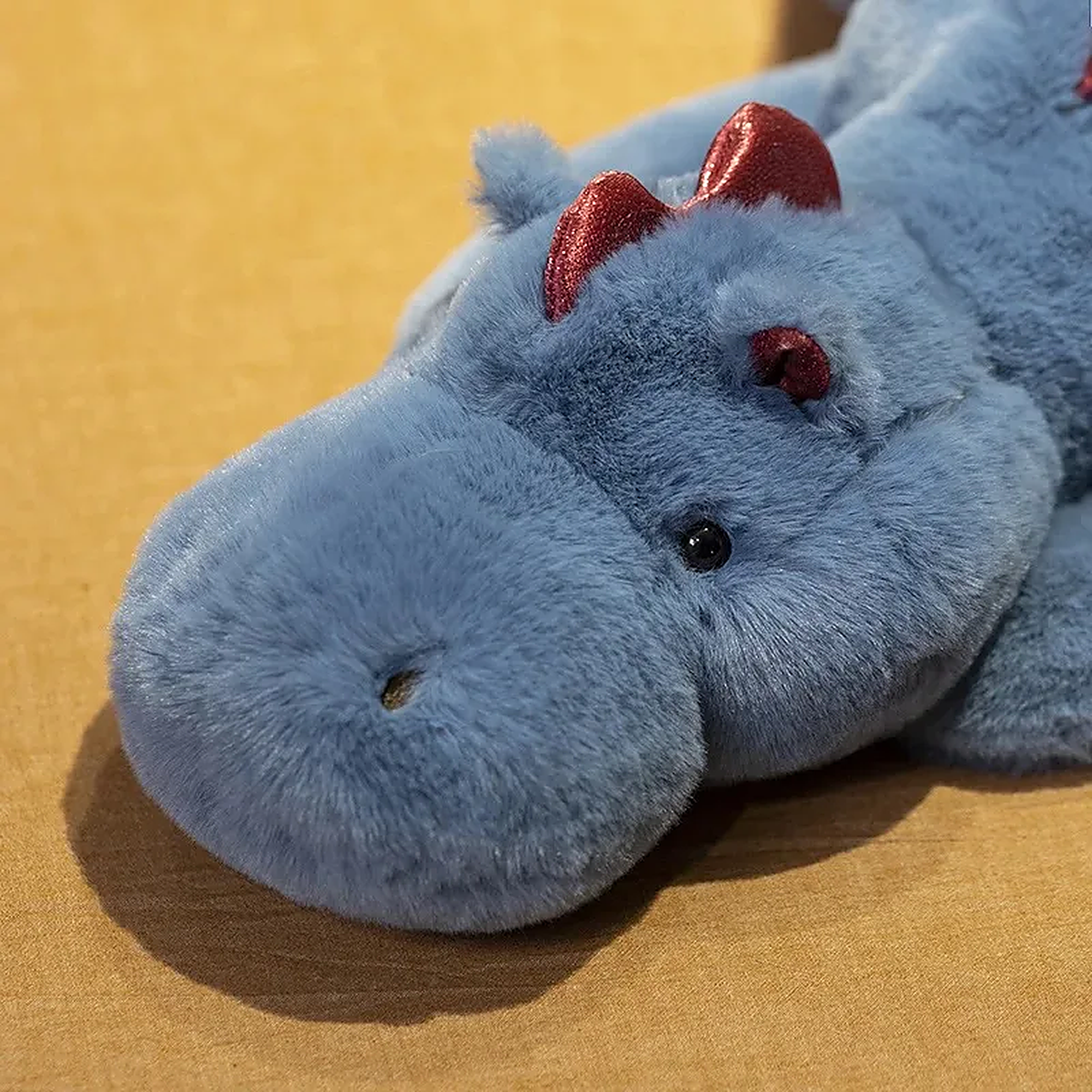 Blue dragon plush toy with red accents, featuring a round head and soft body, resting on a brown surface.