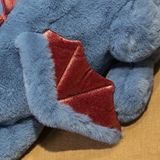 Close-up of a blue plush dragon toy with red wings and soft fur texture.