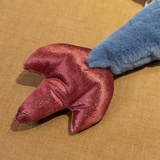 Close-up of a plush dragon's wing with a red and shiny texture, resting on a brown surface.