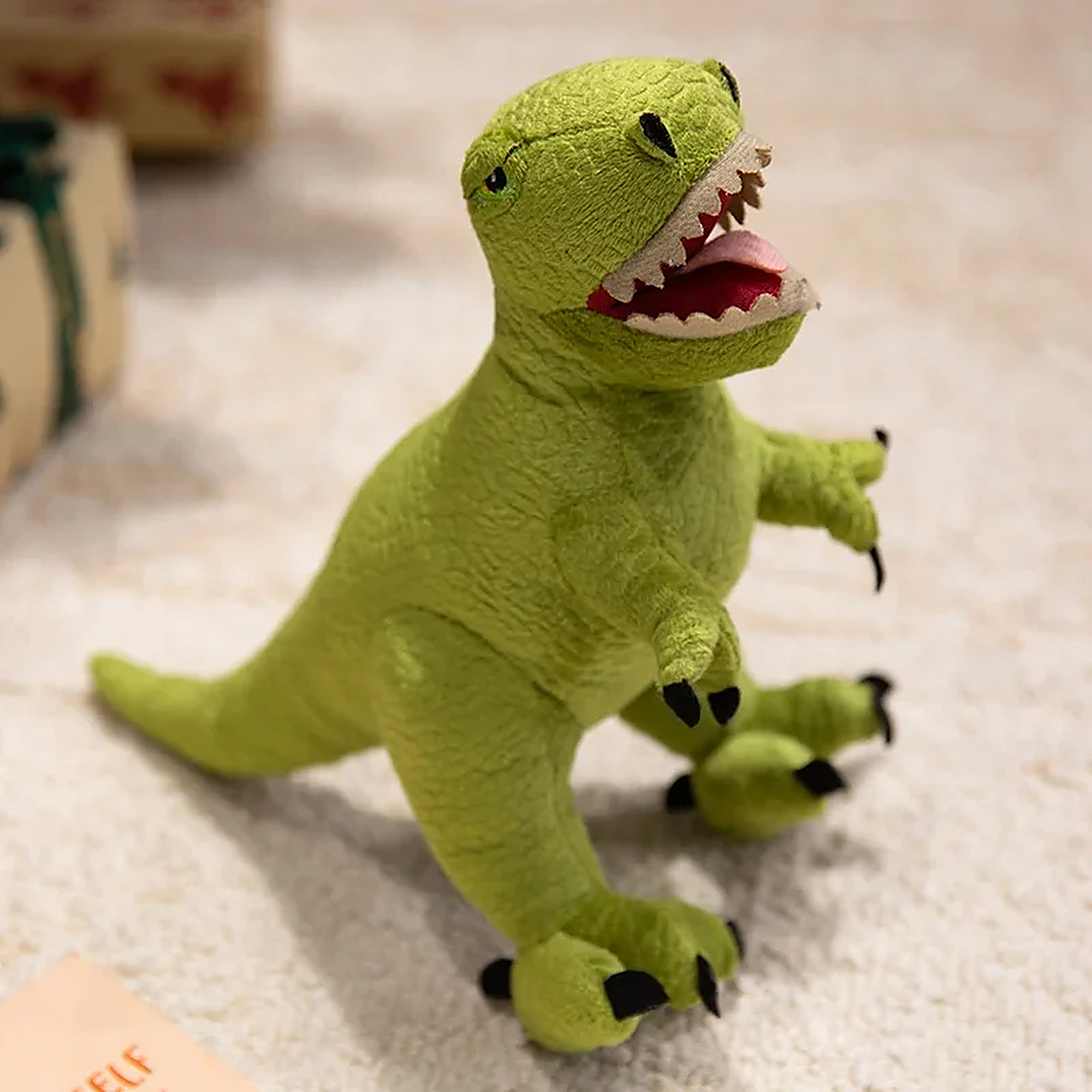 Green plush dinosaur toy with a smiling face and small claws, sitting on a light-colored surface.