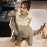 A person holds a plush dinosaur toy resembling a long-necked dinosaur in a cozy indoor setting.
