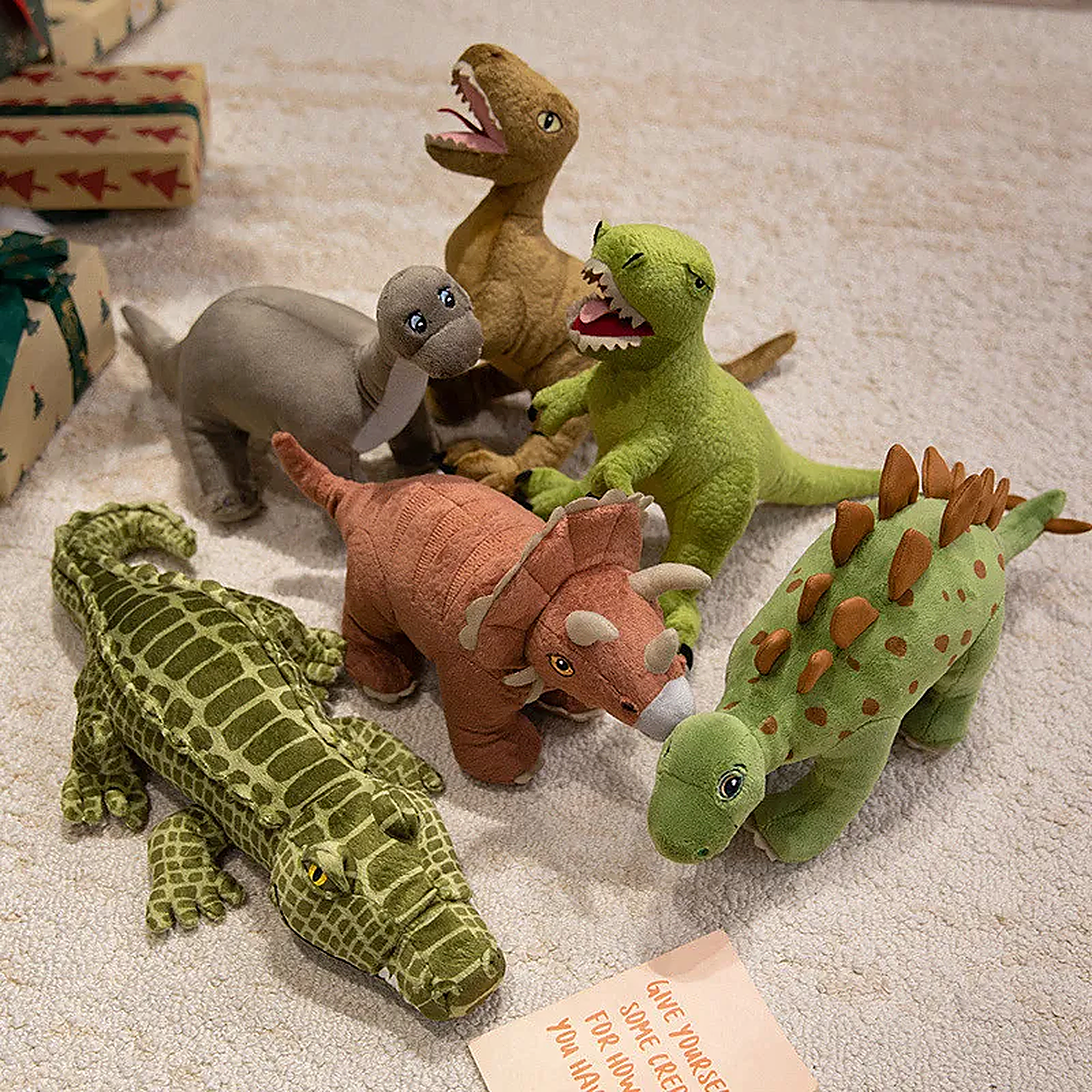 A collection of six plush dinosaur toys in various colors and styles on a soft surface, with a note nearby.