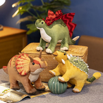 Three plush dinosaur toys in various colors and designs, sitting on a table with a decorative item nearby.