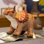 Plush triceratops toy with colorful details, sitting on a magazine in a cozy room setting.