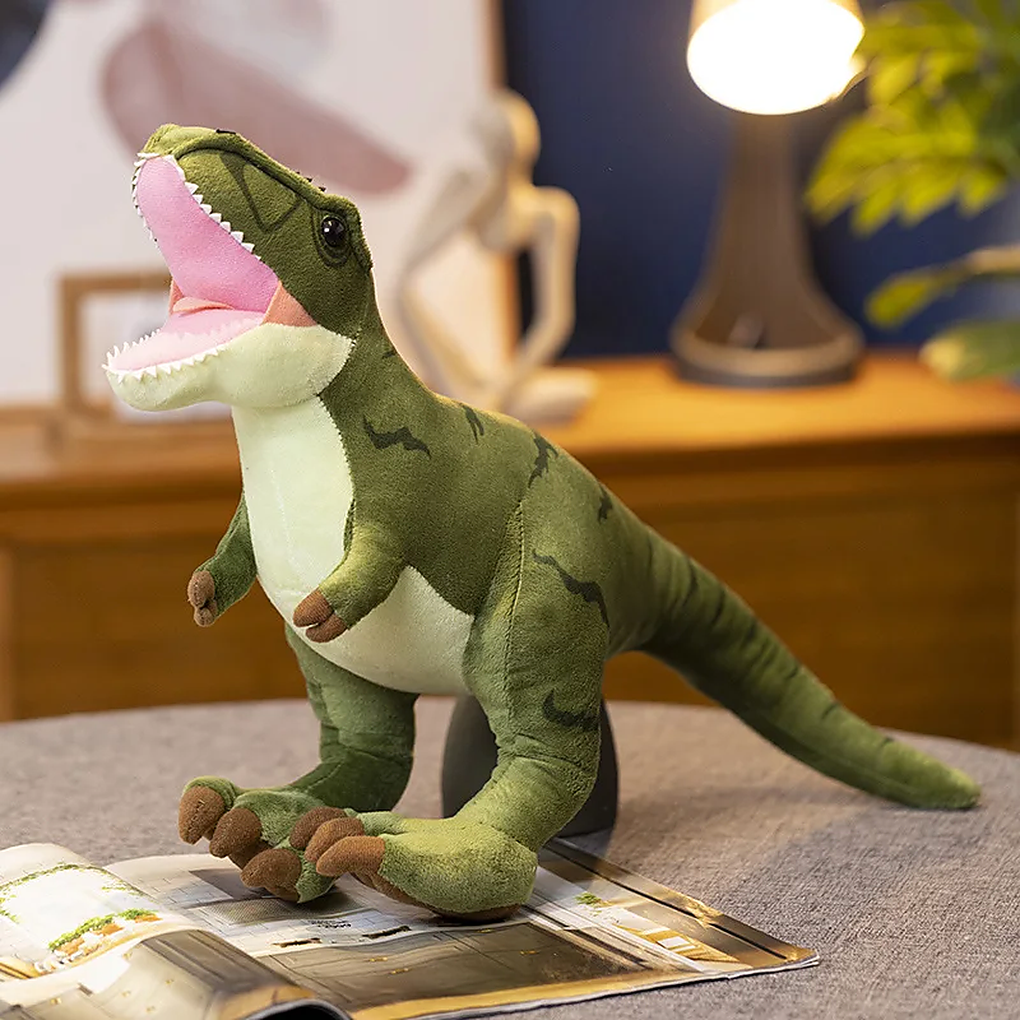 Plush Tyrannosaurus Rex toy with a green body and pink mouth, sitting on a magazine in a cozy room setting.