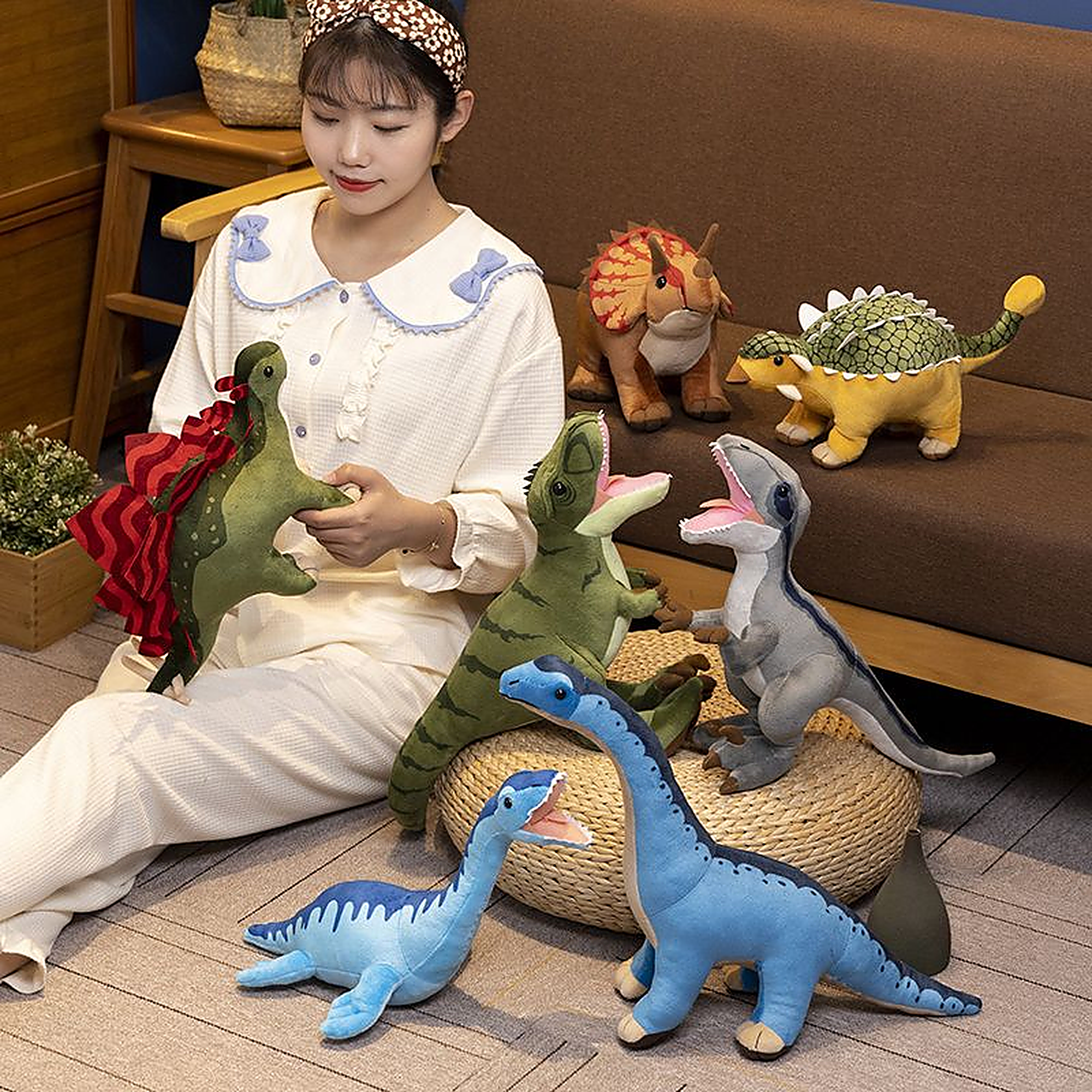 A person sits on the floor surrounded by various plush dinosaur toys in a cozy indoor setting.