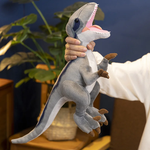 A person holds a plush dinosaur toy, featuring a gray Tyrannosaurus Rex with a smiling mouth and detailed limbs.