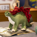 Soft green dinosaur plush toy with a red frill, sitting on a magazine in a cozy room setting.