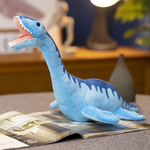 Blue plush dinosaur toy with a smiling face, sitting on a magazine in a cozy room setting.