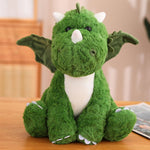 Green plush dinosaur with wings sitting on a wooden surface.