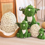 Green dinosaur plush toys in various sizes next to a speckled dragon egg-shaped pillow.
