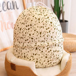 Plush dinosaur egg-shaped pillow with a speckled design, resting on a soft cushion in a cozy setting.