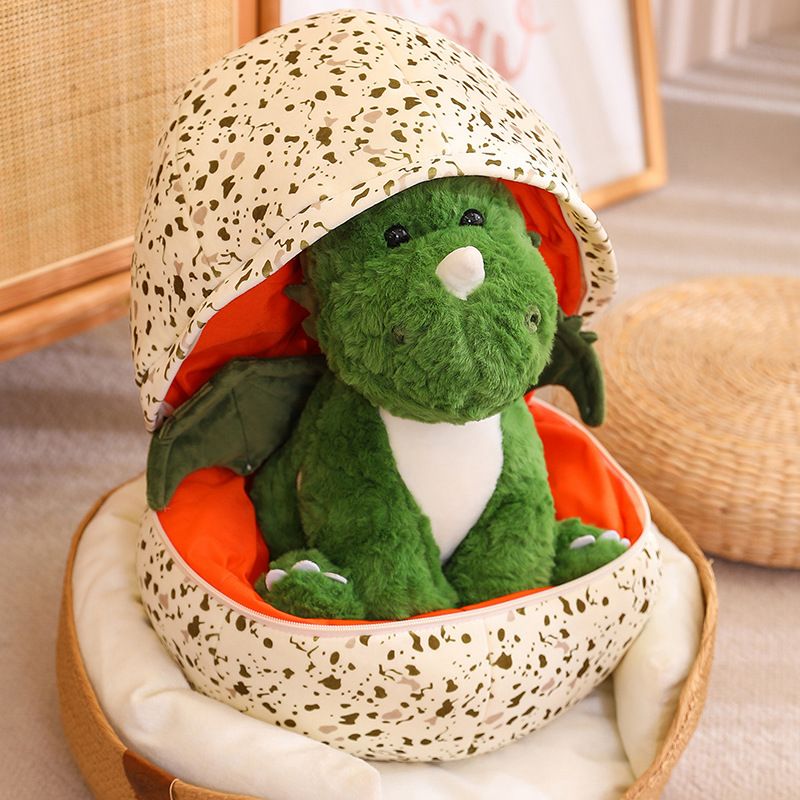 Green plush dinosaur with wings inside a spotted egg-shaped pillow.