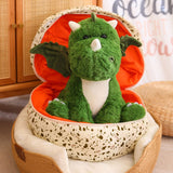 Green dinosaur plush toy with wings sitting inside a patterned egg-shaped pillow.