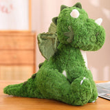 Green plush dinosaur with small wings and spikes, sitting on a wooden surface.