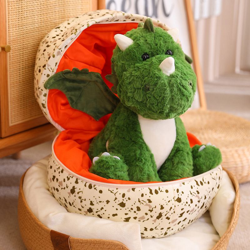 Green plush dinosaur with wings sitting inside a speckled dragon egg-shaped pillow.