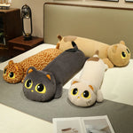 Long plush pillows shaped like cats in various colors and patterns, displayed on a bed with a gray blanket.