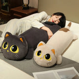 A person lies on a bed hugging two long cat-shaped plush pillows in different colors.