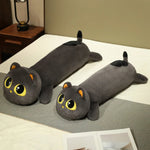 Plush long cat pillow with large eyes, gray fur, and orange ears, resting on a bed with a gray blanket.