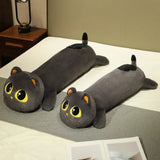 Plush long cat pillow with large eyes, gray fur, and orange ears, resting on a bed with a gray blanket.