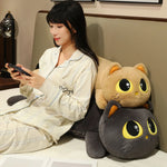 Woman in pajamas sitting on a bed with two large cat plush pillows behind her.