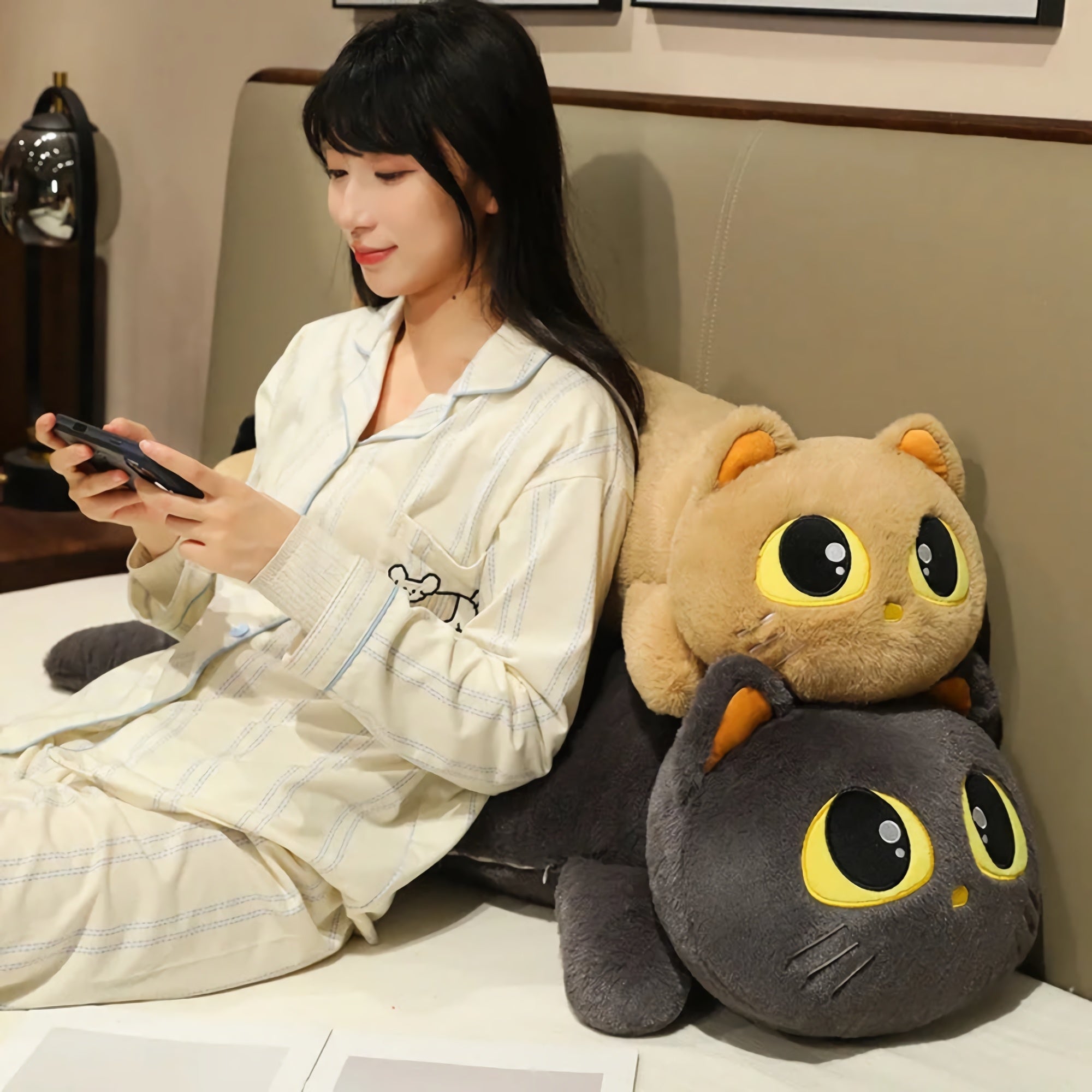 Woman in pajamas sitting on a bed with two large cat plush pillows behind her.