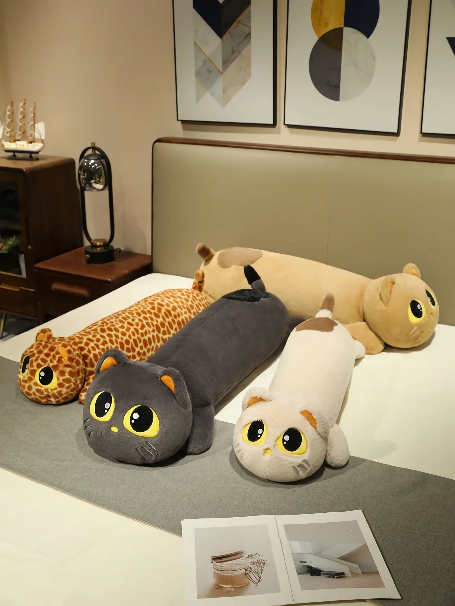 Four long plush pillows resembling cats and a giraffe, arranged on a bed with decorative items nearby.