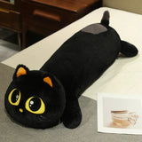 Black cat-shaped plush pillow with large yellow eyes and orange ears on a bed.