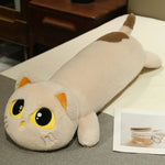 Plush cat-shaped pillow with large eyes and a long body, lying on a bed next to a small photo.