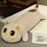 Plush cat-shaped pillow with large eyes and a long body, lying on a bed next to a small photo.