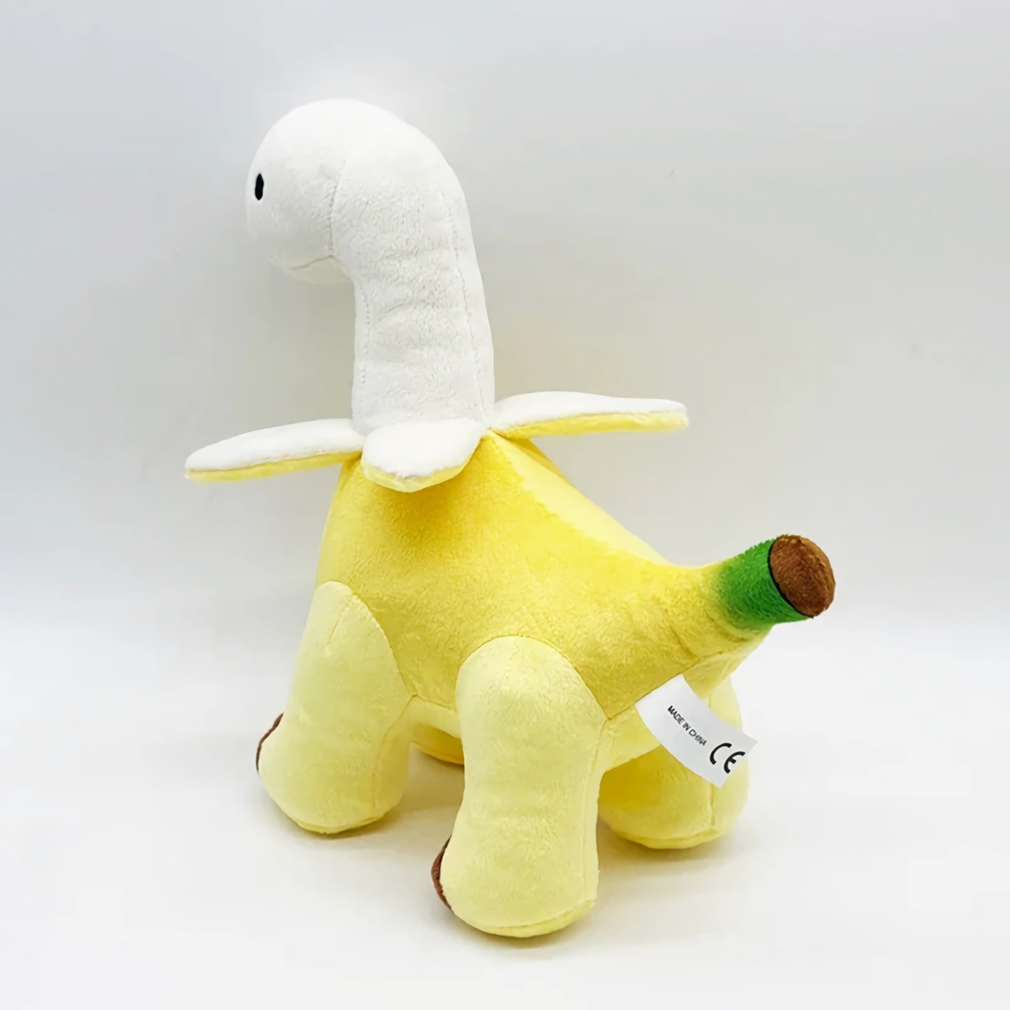 Plush toy resembling a dinosaur with a banana body and a white neck, featuring a green tail and brown feet.