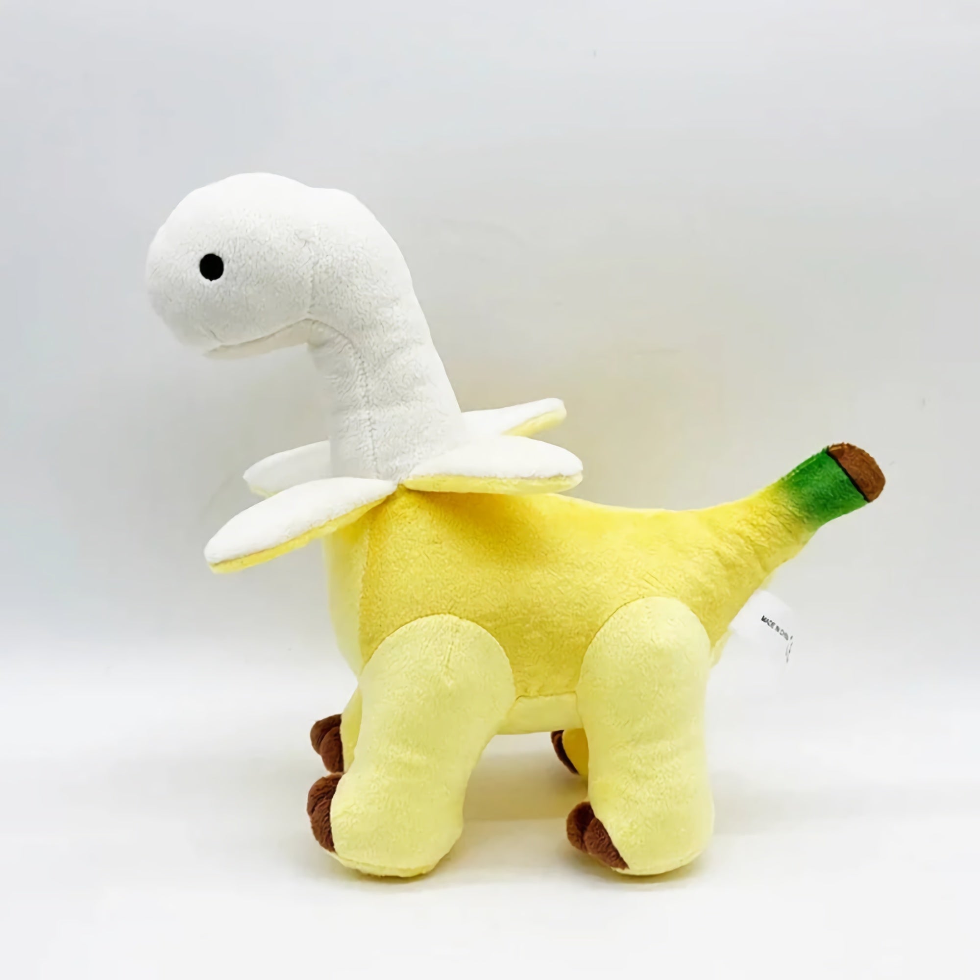 Plush toy resembling a dinosaur with a yellow body, white neck, and green tail, featuring brown feet.