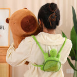A person holds a large brown capybara plush while wearing a green turtle-shaped backpack.