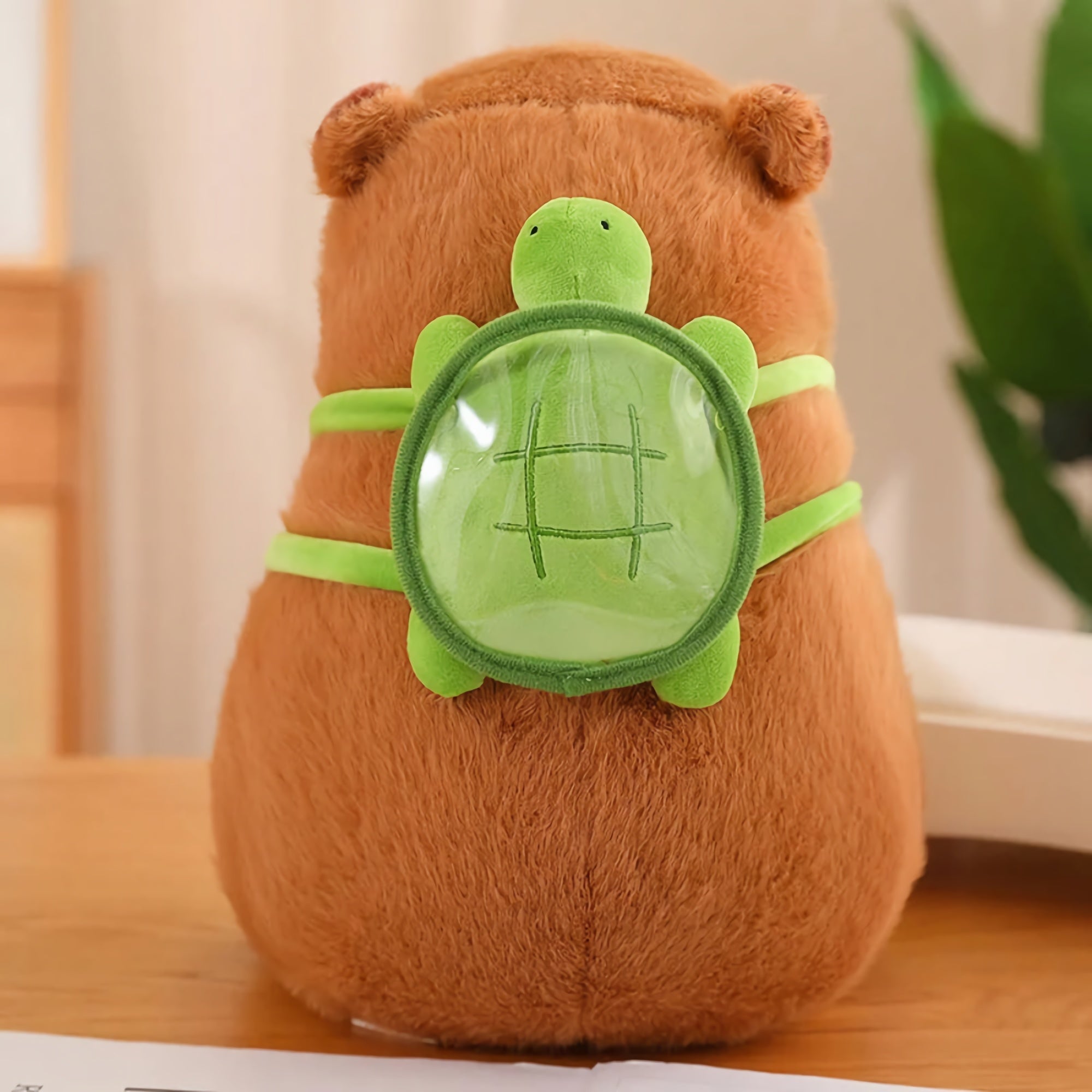 Brown capybara plush with a green turtle-shaped backpack on a wooden surface.